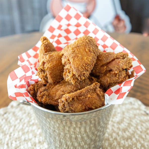 Crispy fried chicken wings in a metal bucket lined with red and white checkered paper.