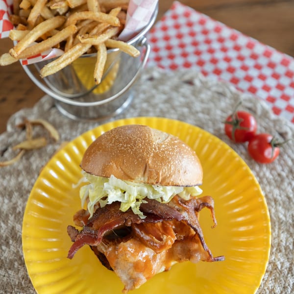 Smoke Shack BBQ sandwich with bacon, cheese, and lettuce on a yellow plate with fries.