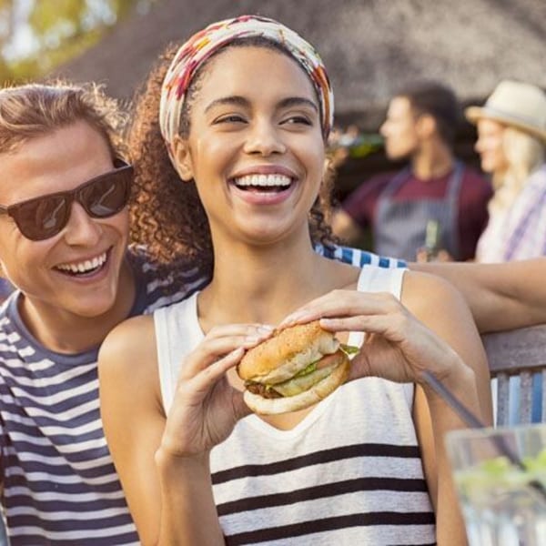 Smiling woman holding a Smoke Shack BBQ burger, with a man in sunglasses beside her.