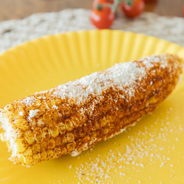 Elote, Mexican street corn, on a yellow plate, topped with spices and cotija cheese.