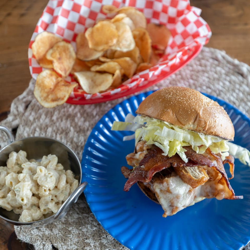 Smoke Shack BBQ sandwich with bacon, lettuce, and melted cheese, served with chips and macaroni.