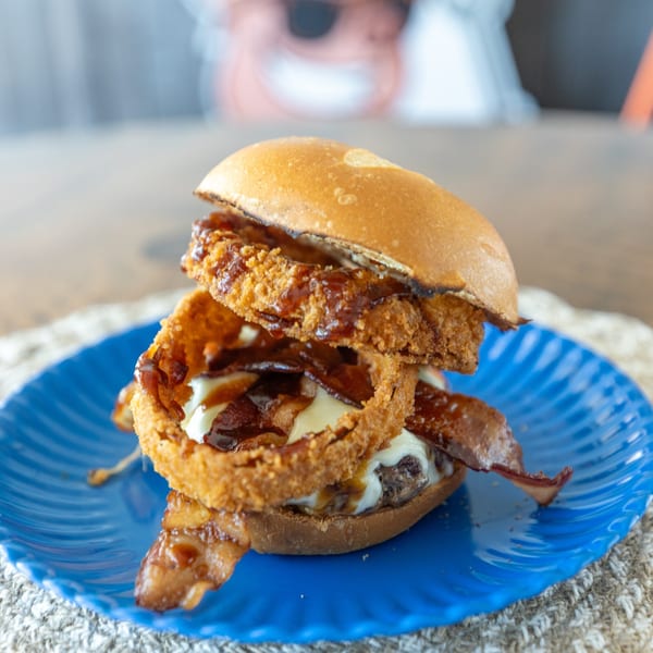 A Smoke Shack BBQ burger with onion rings, bacon, and BBQ sauce on a blue plate.