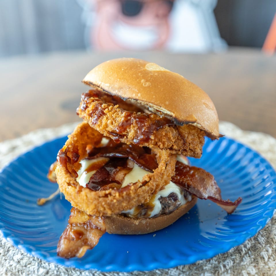 A Smoke Shack BBQ burger with onion rings, bacon, and BBQ sauce on a blue plate.