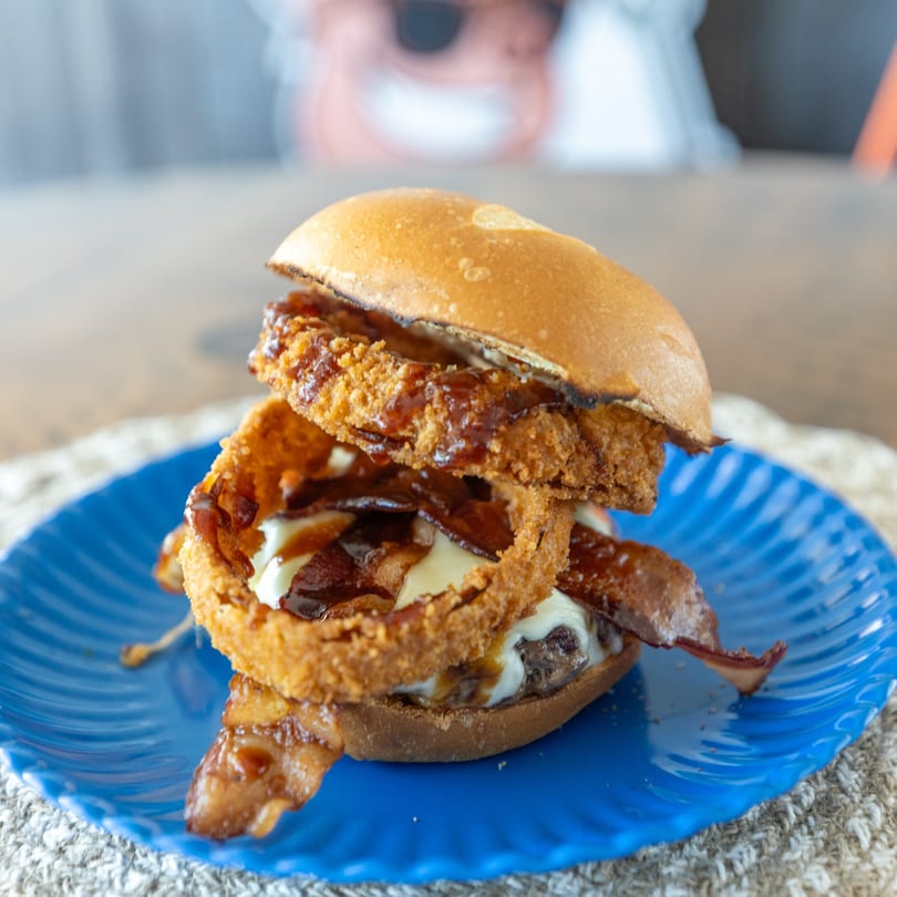 A Smoke Shack BBQ burger with onion rings, bacon, and BBQ sauce on a blue plate.