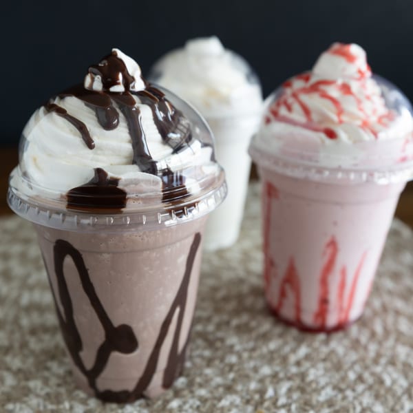 Three milkshakes, chocolate, vanilla, and strawberry, topped with whipped cream and syrup.